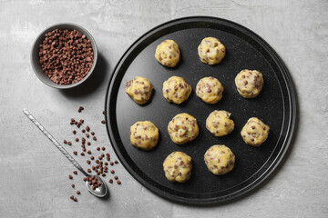 Tray with raw chocolate chip cookie balls and spoon on gray table, flat lay