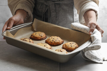 Woman putting baking pan with chocolate chip cookies on table, closeup