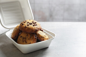 Delicious chocolate chip cookies in plastic container on light table, closeup. Space for text