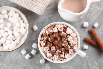 Cup of aromatic hot chocolate with marshmallows, and cocoa powder served on gray table, flat lay