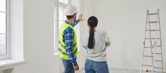 Professional repairman explaining future home design plan to young woman. View from behind of...