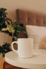 White coffee cup on the table in sunny morning bedroom, mock up.