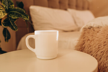 White coffee cup on the table in sunny morning bedroom, mock up.