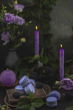 Violet macarons and blackberries on dark green background. Purple candles and Eustoma or lisianthus. Delicious french delicate dessert