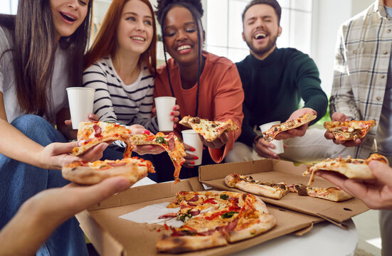 Happy young diverse multiethnic people friends or colleagues having party gathering at home eating slices of pizza from box, talking and laughing together. Delivery service concept. - Powered by Adobe