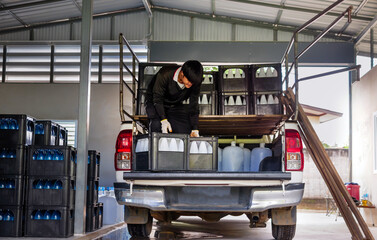 Workers lift white drinking water bottles in crates into the back of a transport truck purified drinking water inside the production line to prepare for sale. Water drink factory, small business