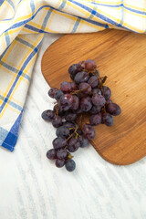 Cutting board with bunch of organic black grapes on white wooden background..