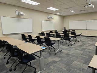 Empty classroom interior, with rows of desks and a projector suspended from the ceiling