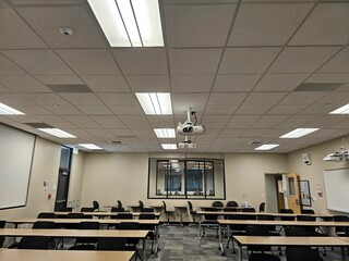 Empty classroom interior, with rows of desks and a projector suspended from the ceiling