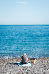 une femme assise seule sur la plage face &agrave; la mer. Une personne de dos sur la plage de m&eacute;diterran&eacute;e. Femme face &agrave; l'horizon. Vacances &agrave; la mer. Seule sur la plage. Se d&eacute;tendre &agrave; la mer. Relaxation. 
