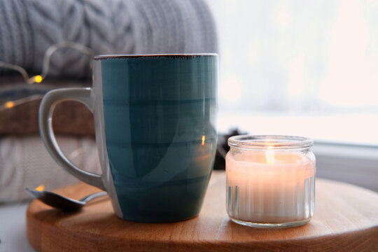 Winter windowsill still life. Blue ceramic cup of hot coffee on window sill. Christmas decorations on the background. Cozy home picture. Warm woolen knitted sweaters, Burn Candle, Cookies. Stock photo