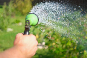 Gardener with a watering hose. Person spraying green grass lawn with hose sprayer. Irrigation with...