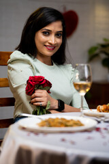 Vertical shot of happy girl with red roses looking at camera during candlelight dinner at restaurant - concept of valentines day, anniversary and dating