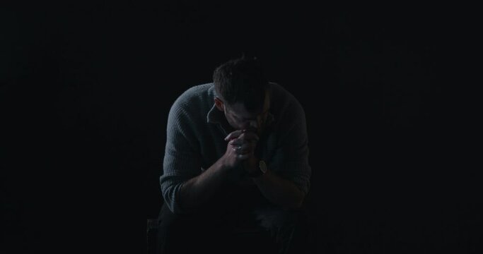 Depressed man sits in darkness shaking head