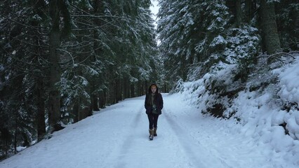 A young woman walks towards the camera on a dark, ominous snow covered path in the Vosges Forest. 