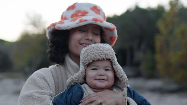 Portrait of cool Asian mom bouncing her adorable infant baby in winter sunset. Slow motion