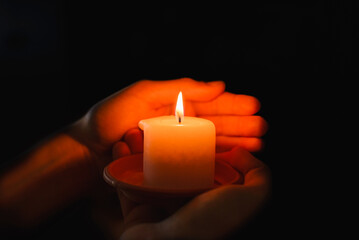 Religious concept.Boy holds in a hand a burning candle against black background.