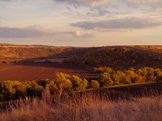 Fototapeta premium Plowed fields in a valley between hills at sunset. Autumn agronomic landscape.