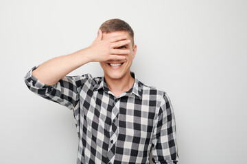 Portrait of young businessman covering eyes with hand, peeking through fingers isolated on white studio background.