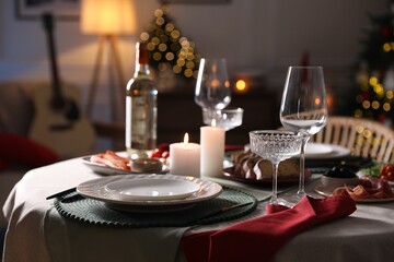 Christmas table setting with burning candles, appetizers and dishware indoors