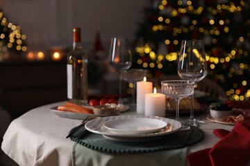 Christmas table setting with burning candles, appetizers and dishware indoors