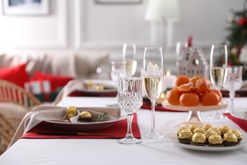 Christmas table setting with tangerines, candies and dishware indoors