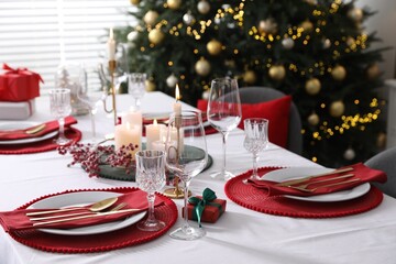 Christmas table setting with burning candles, gift box and dishware indoors