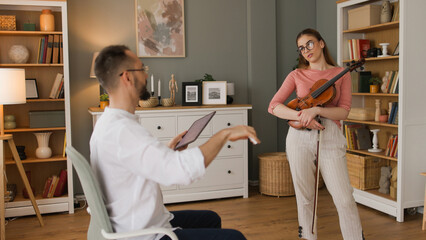 Male music teacher giving private violin lessons to a teenage girl - obrazy, fototapety, plakaty
