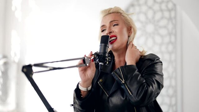 sexy blonde woman with red lips singing song to microphone in studio with white background, portrait
