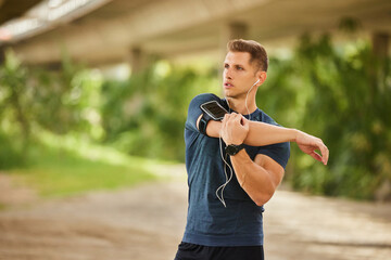 Young man stretching arm under bridge before workout outdoors