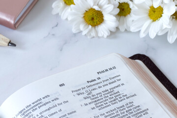 Open holy bible book, Psalm 10 verses with flowers on white marble table. Close-up. Selective...