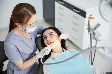 Beautiful young woman doing tooth examination in the dental office. Portrait of smiling girl on a dental chair in dentistry - obrazy, fototapety, plakaty