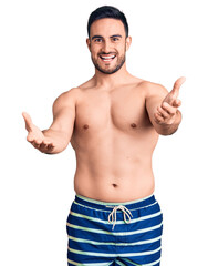 Fototapeta premium Young handsome man wearing swimwear smiling cheerful offering hands giving assistance and acceptance.