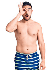 Fototapeta premium Young handsome man wearing swimwear doing ok gesture shocked with surprised face, eye looking through fingers. unbelieving expression.