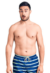 Fototapeta premium Young handsome man wearing swimwear in shock face, looking skeptical and sarcastic, surprised with open mouth