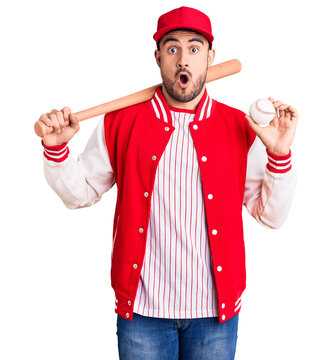 Young handsome man holding baseball bat and ball scared and amazed with open mouth for surprise, disbelief face