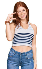 Young read head woman wearing casual clothes smiling and confident gesturing with hand doing small size sign with fingers looking and the camera. measure concept.