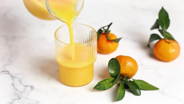 Pouring orange juice into a glass from a jug, tangerines with leaves, a refreshing drink. Horizontal video.