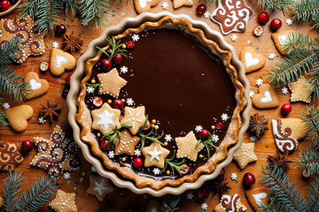 Christmas gingerbread and chocolate tart decorated with small stars-shaped gingerbreads, cranberries and rosemary in a baking dish, top view