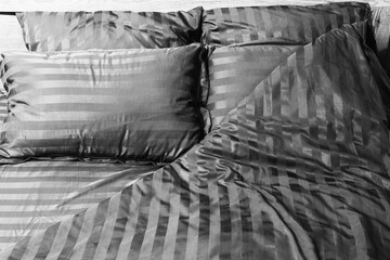 empty spread bed with striped satin bed linen close-up, black and white photo
