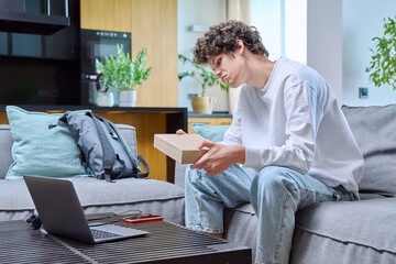 Young male unpacking an online purchase, sitting on couch at home