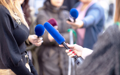 Press, news conference or media scrum, female journalist holding microphone, other reporters with microphones in the background
