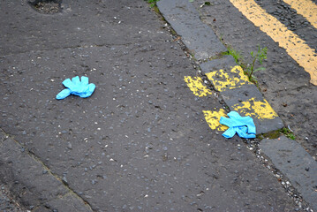 Discarded Blue Latex Rubber Gloves on Textured Grey Tarmac Road Surface with Yellow Painted Traffic Markings 