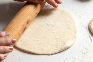 Woman's hands holding wooden rolling pin on dough with flour on kitchen table. Preparation for...