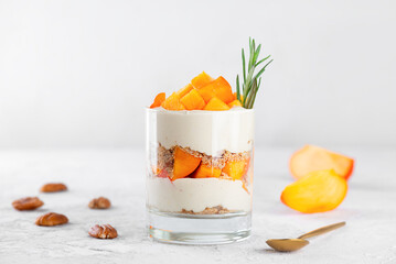 Trifle in a glass with persimmon, rosemary, pecan, whipped cream and biscuit. Healthy food, vegan,...