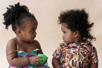 Two Nigerian girls, ages 2 and 1, with beautiful curly hairstyles on a colored background. African...