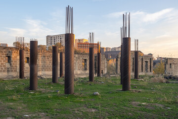 Abandoned construction site. Columns with protruding reinforcement. Construction of house is temporarily frozen. Construction site overgrown with grass. Abandoned walls from unfinished building