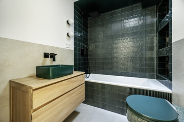 A bathroom with green stoneware in the bathtub and cream-colored tiles in the rest, a shower cabin...