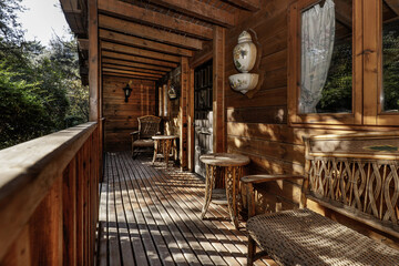 Front porch of a wooden cabin with wooden and wicker furniture and views of a plot with lush trees