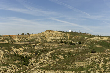 Landscape of a mountain with eroded material and a white geodesic dome covering radars